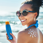 Portrait of a beautiful young woman with a sun drawn on her shoulder with sunscreen at the beach