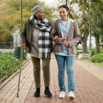 Help, cane and nurse with old woman in park for relax, support and person with a disability. Elderly care, conversation and healthcare with caregiver and patient in nature for medical rehabilitation