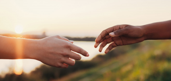 African and caucasian women reaching out their hands to each other