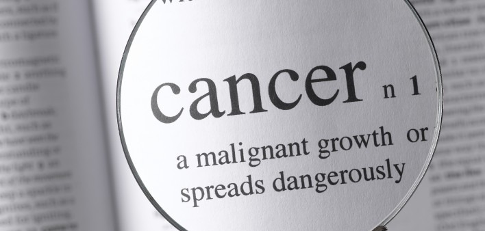 a magnifying glass magnifying the definition of cancer in a dictonary