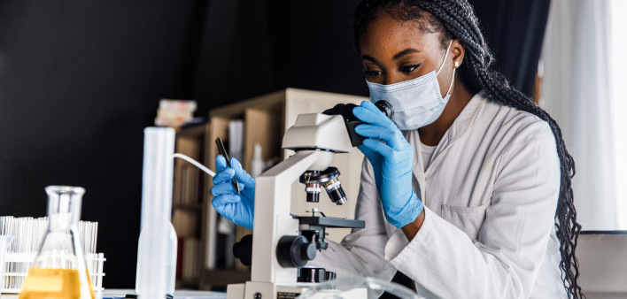 female scienitst analyzing a sample under a microscope while doing research