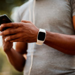 African-American male with smart watch and headphones texting messages on mobile phone during jogging session.