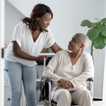 A young woman pushes her mother in a wheelchair through the house as she comes to help and support through her Cancer journey.