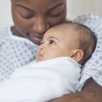 Beautiful African American mother in a hospital gown holds her newborn baby