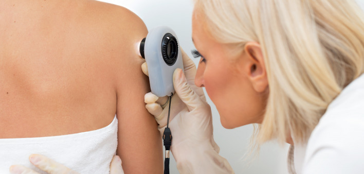 Female dermatologist examining female patient's skin with dermascope, doctor is carefully looking for signs of skin cancer