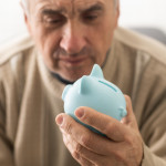 Senior caucasian man holding piggy bank with glasses depressed and worry for distress, crying angry and afraid.
