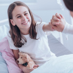 High angle of girl with plush toy smiling and giving a high five with nurse in the hospital
