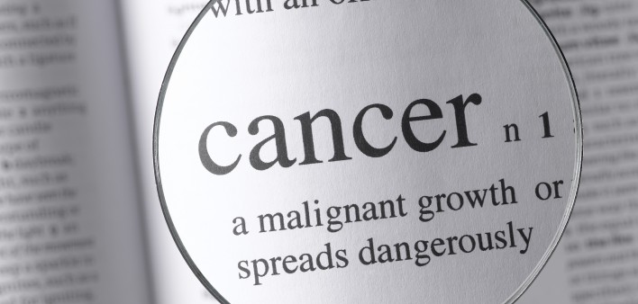 a magnifying glass magnifying the definition of cancer in a dictonary