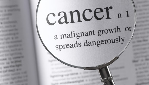 a magnifying glass magnifying the definition of cancer in a dictonary
