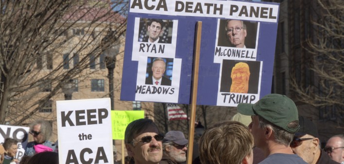 Obamacare activists hold signs saying Republicans Mark Meadows, Paul Ryan, Mitch McConnell and President Trump are the real ACA Death Panel