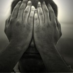 a black and white image of a man holding his hands over his face