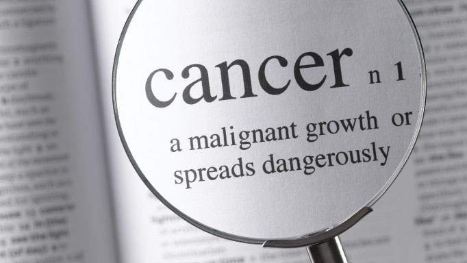 a magnifying glass magnifying the definition of cancer in a dictonary