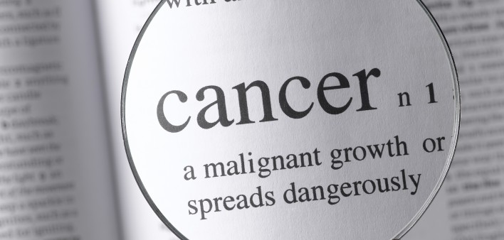 a magnifying glass magnifying the definition of cancer in a dictonary