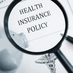 A maginfying glass looking at the words "Health Insurance Policy"