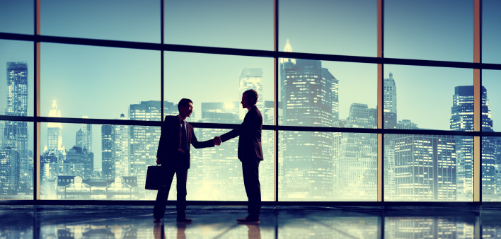  Businessmen shake hands in front of windows and skyline at night