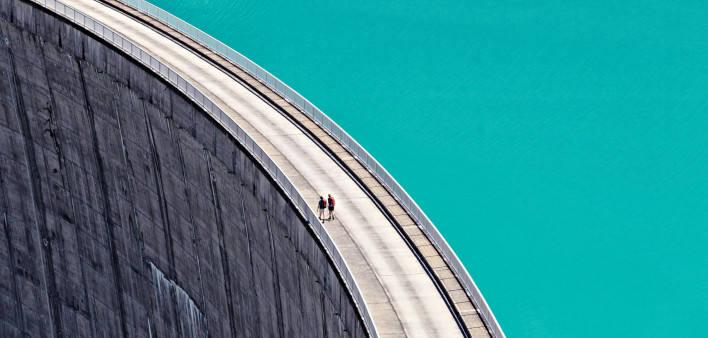 two small figures walking on huge Dam