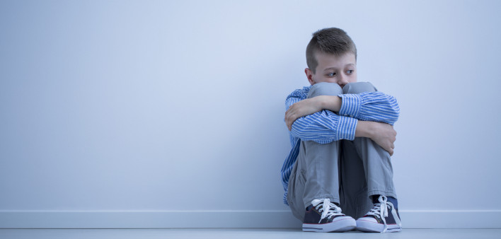 Young boy with hypersensitivity sitting alone on the floor against the wall