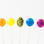 Lollipops in the colors of the rainbow, with a green marijuana bud on a lollipop stick in the middle.