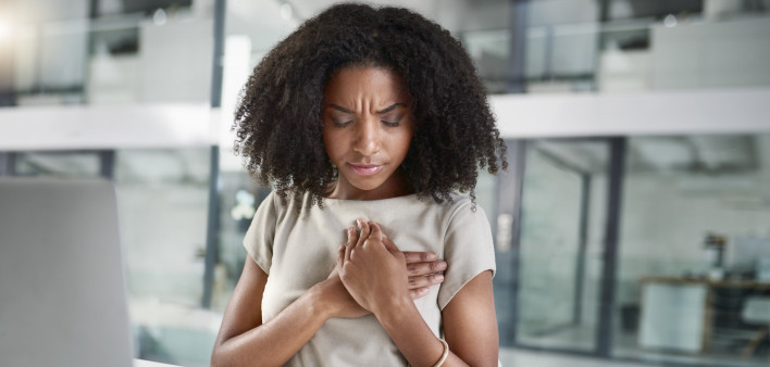 Cropped shot of an attractive young businesswoman holding her chest in pain while sitting in her office