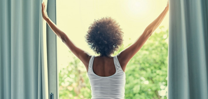 woman parting curtains of window in the morning