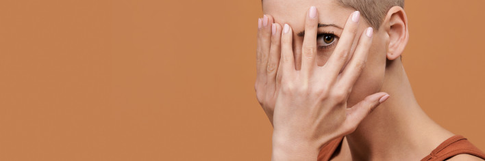 Beautiful young woman with shaved head covering her face with both hands