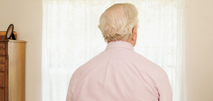 older man sitting on bed with back to camera