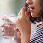 woman taking a pill and holding a glass of water