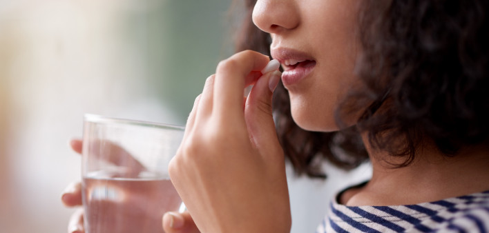 woman taking a pill and holding a glass of water