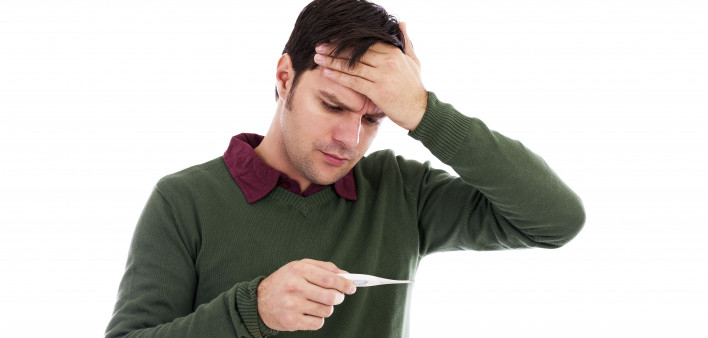 Young man holding his hand to his forehead and holding a thermometer