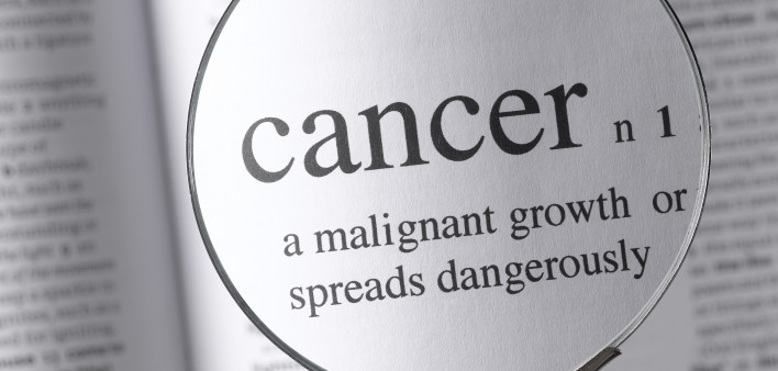 a magnifying glass magnifying the definition of cancer in a dictonary