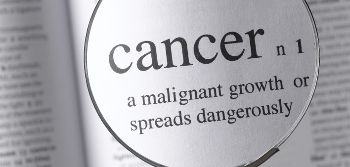 a magnifying glass magnifying the definition of cancer in a dictonary