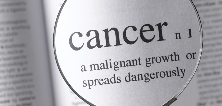 a magnifying glass magnifying the definition of cancer in a dictonary