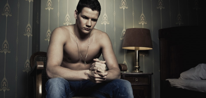 a shirtless man sitting in a bedroom at night