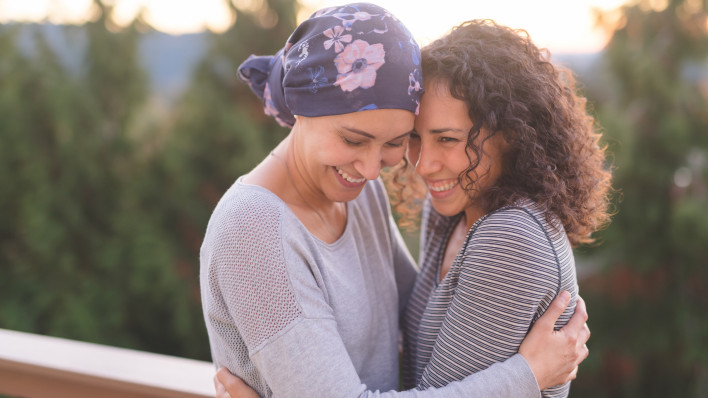 Beautiful ethnic woman battling cancer hugs her sister tightly