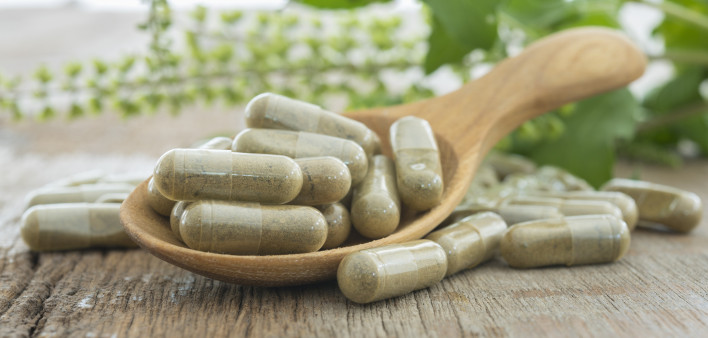 herb capsules in wooden spoon on table