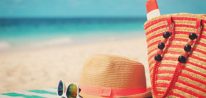 beach bag, sun glasses, sun hat on towel at beach ocean in the background