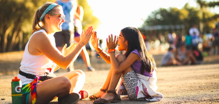 A counselor and a young camper play pattycake.