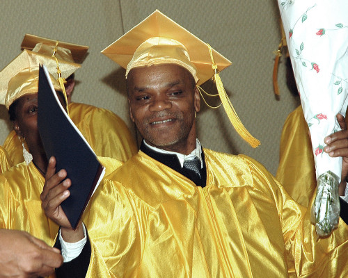 A graduate clutches his diploma proudly, a bouquet of flowers in his other hand.