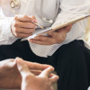 a doctors hands taking notes, sitting with patient