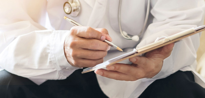 a doctors hands taking notes, sitting with patient