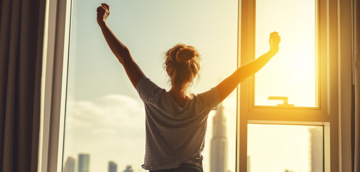 happy woman stretches and opens the curtains at window in morning