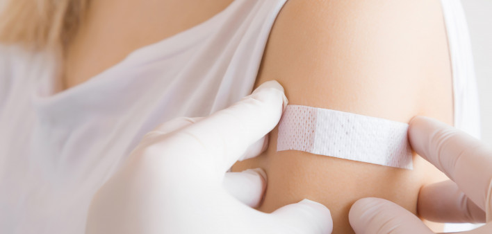 Doctor in white rubber protective gloves putting an adhesive bandage on young woman's arm after scratch on skin or injection of vaccine