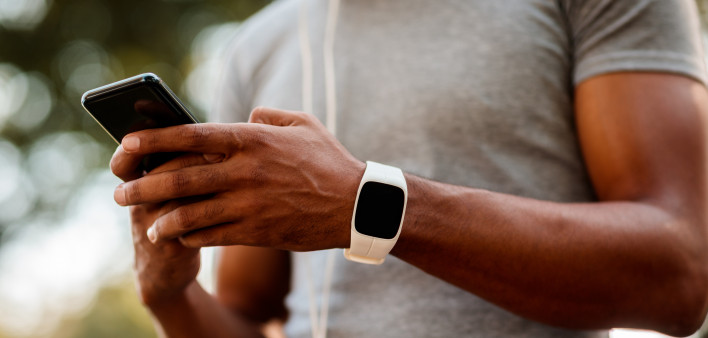 African-American male with smart watch and headphones texting messages on mobile phone during jogging session.