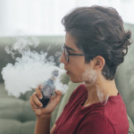 Young man vaping e-cigarette at home