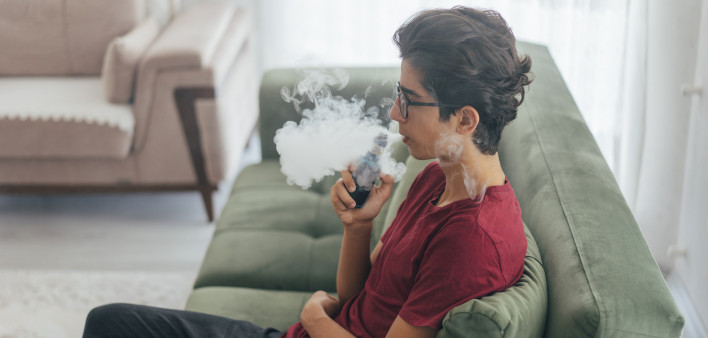 Young man vaping e-cigarette at home