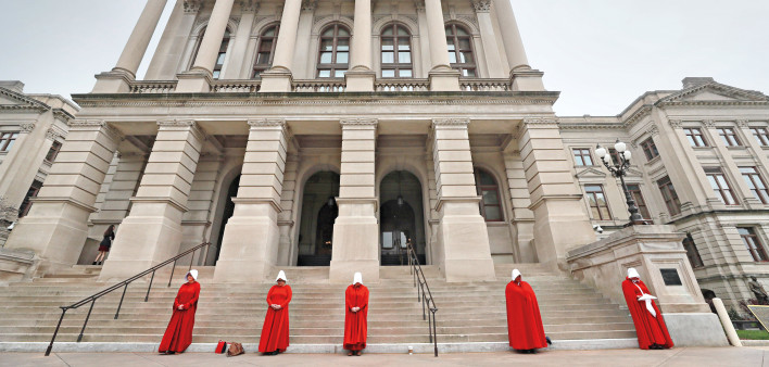 woman dressed in handmaids tale red outfits protest cuts to abortion funding