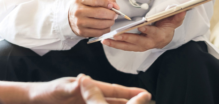a doctors hands taking notes, sitting with patient