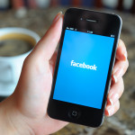 Woman hand holding an Apple iPhone 4 in a coffee shop. iPhone 4 displaying start up screen of Facebook application.