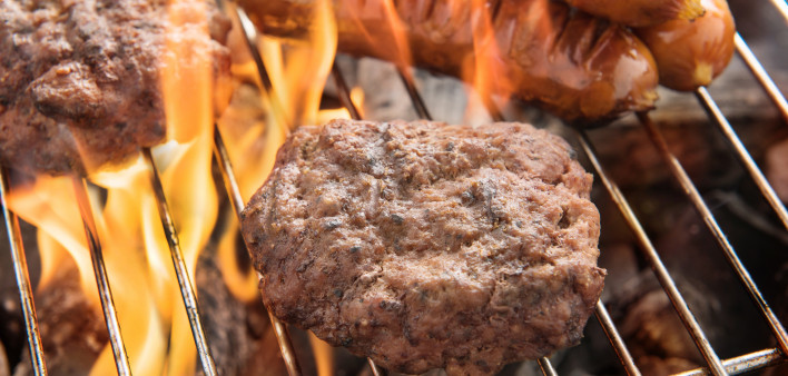 hotdogs and hamburgers on a grill with flames