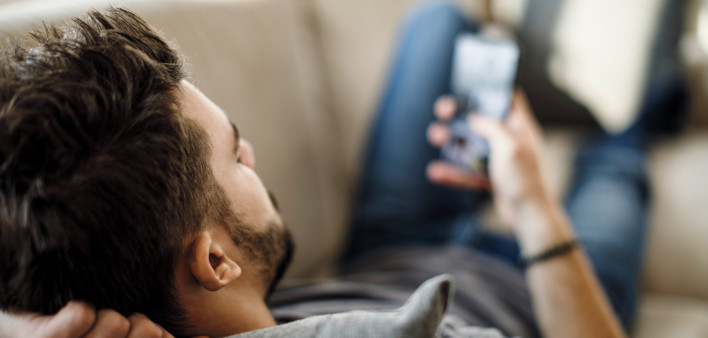 man on couch texing on smart phone